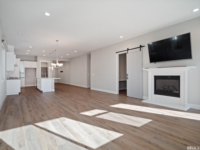 unfurnished living room featuring sink, light hardwood / wood-style flooring, a barn door, and a chandelier