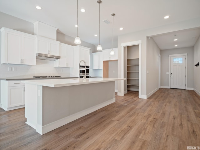 kitchen featuring pendant lighting, an island with sink, decorative backsplash, light wood-type flooring, and white cabinets