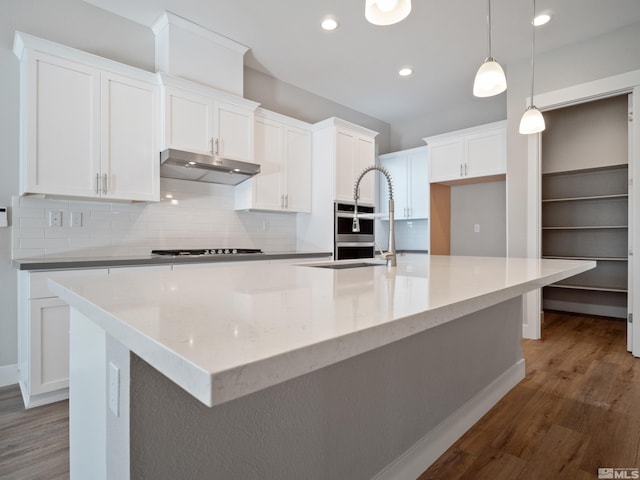 kitchen with a spacious island, hardwood / wood-style flooring, white cabinets, decorative light fixtures, and gas cooktop