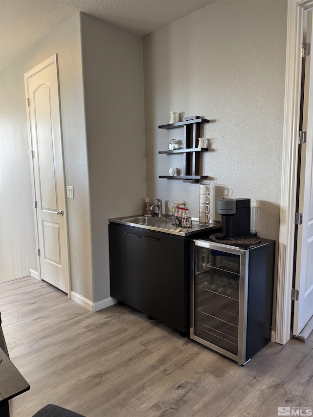 bar featuring a textured ceiling, light hardwood / wood-style flooring, and wine cooler