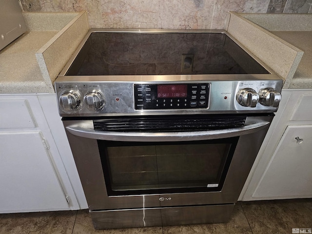 interior details with stainless steel range with electric stovetop and white cabinetry