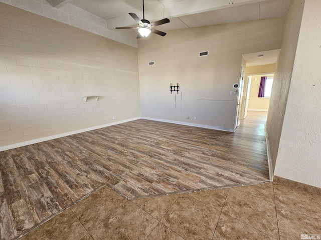 empty room with ceiling fan, hardwood / wood-style floors, vaulted ceiling, and brick wall