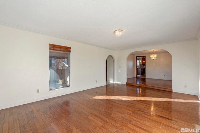 spare room featuring a textured ceiling, a notable chandelier, crown molding, and hardwood / wood-style floors