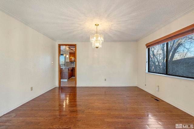 empty room with wood-type flooring, a textured ceiling, a chandelier, and ornamental molding