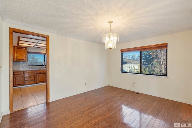 empty room featuring crown molding, an inviting chandelier, light hardwood / wood-style floors, and a textured ceiling