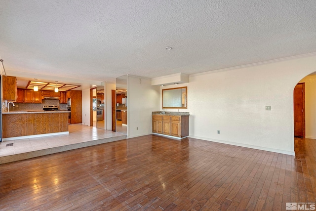 unfurnished living room with light hardwood / wood-style floors, ornamental molding, sink, and a textured ceiling