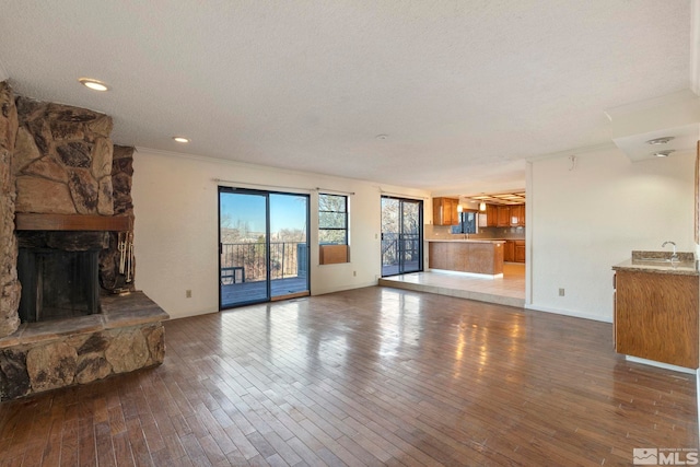 unfurnished living room featuring a textured ceiling, a stone fireplace, crown molding, and dark hardwood / wood-style floors