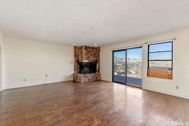 unfurnished living room featuring a textured ceiling, hardwood / wood-style floors, a mountain view, crown molding, and a stone fireplace