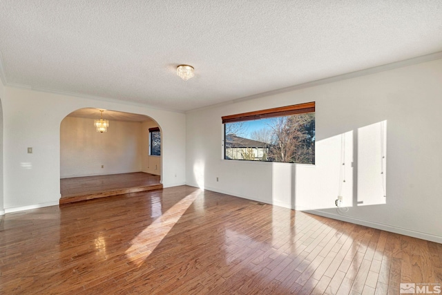 spare room with a textured ceiling, hardwood / wood-style floors, a chandelier, and crown molding