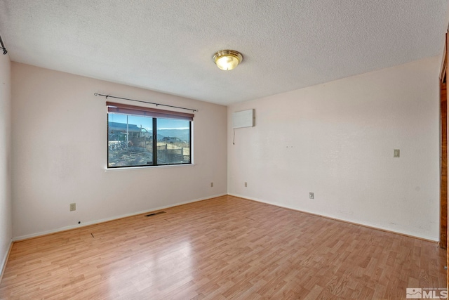 empty room with a textured ceiling and light hardwood / wood-style flooring