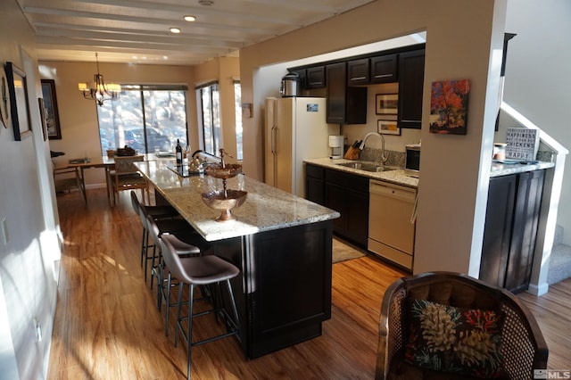 kitchen with white appliances, light stone counters, an island with sink, light hardwood / wood-style floors, and sink