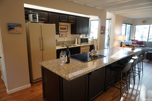 kitchen with light stone countertops, a center island, black electric stovetop, white refrigerator, and sink