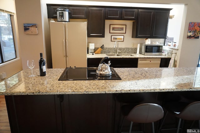 kitchen with white appliances, a kitchen bar, light stone counters, and sink