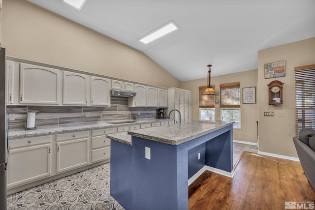 kitchen featuring light stone countertops, vaulted ceiling, pendant lighting, a kitchen island with sink, and backsplash