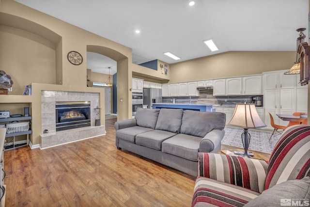 living room with light wood-type flooring, a tile fireplace, and vaulted ceiling