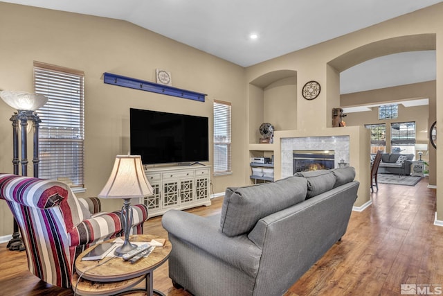 living room with a high end fireplace, lofted ceiling, and hardwood / wood-style flooring