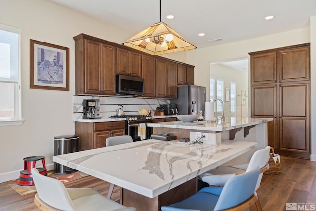 kitchen with a kitchen breakfast bar, a center island with sink, dark hardwood / wood-style flooring, pendant lighting, and appliances with stainless steel finishes