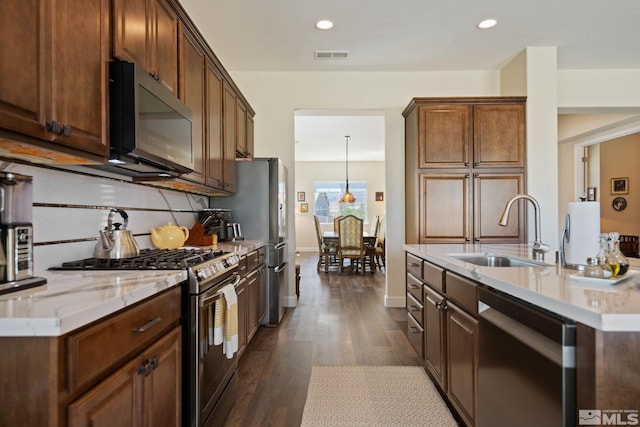 kitchen with appliances with stainless steel finishes, hanging light fixtures, light stone countertops, dark wood-type flooring, and sink