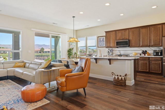 kitchen featuring a breakfast bar area, hanging light fixtures, an island with sink, dark hardwood / wood-style floors, and a mountain view