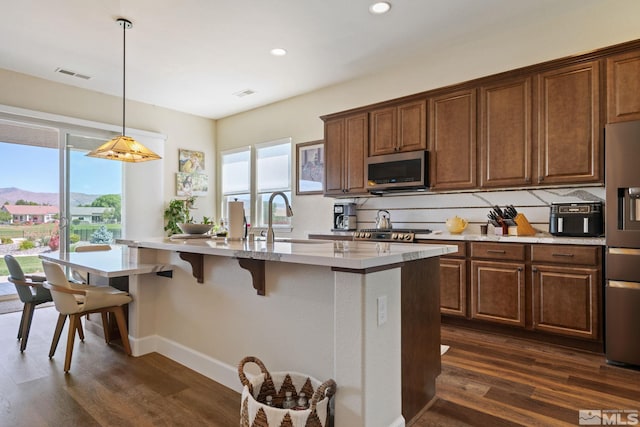 kitchen with stainless steel appliances, sink, hanging light fixtures, a kitchen island with sink, and dark wood-type flooring