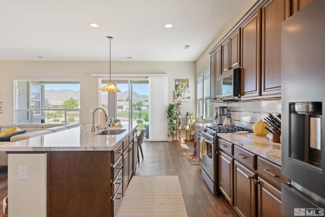 kitchen with a center island with sink, appliances with stainless steel finishes, a mountain view, sink, and decorative light fixtures