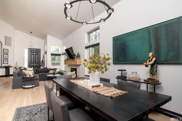 dining space featuring high vaulted ceiling, light wood-type flooring, and an inviting chandelier