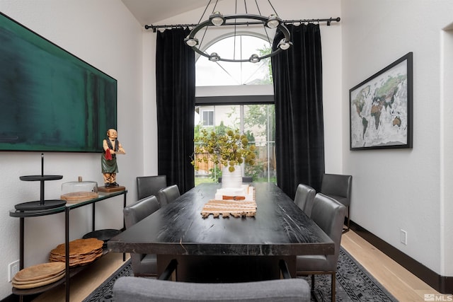 dining space with hardwood / wood-style floors, an inviting chandelier, and lofted ceiling