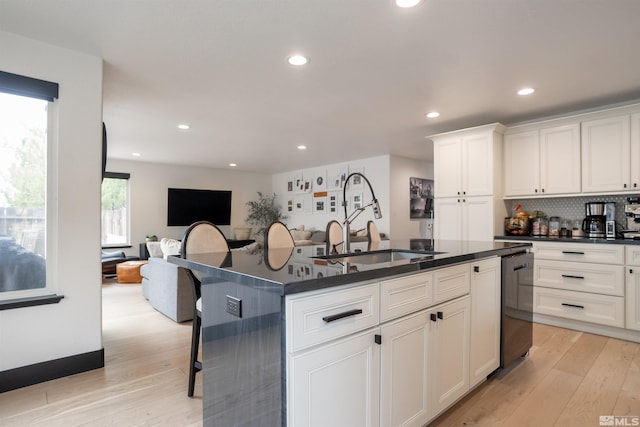 kitchen with a center island with sink, dishwashing machine, light wood-type flooring, white cabinetry, and sink