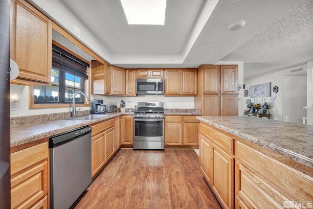 kitchen featuring stainless steel appliances, sink, a textured ceiling, light brown cabinets, and hardwood / wood-style floors