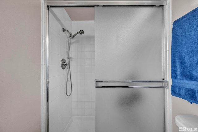 bathroom featuring a shower with door and toilet