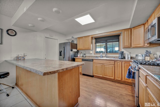 kitchen with appliances with stainless steel finishes, kitchen peninsula, a breakfast bar, light brown cabinets, and sink