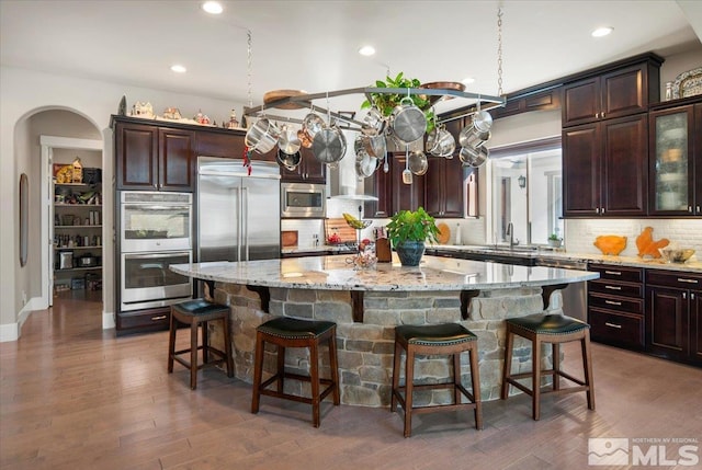 kitchen with built in appliances, a kitchen bar, backsplash, and a spacious island