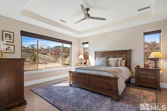 bedroom with ceiling fan, a tray ceiling, and wood-type flooring