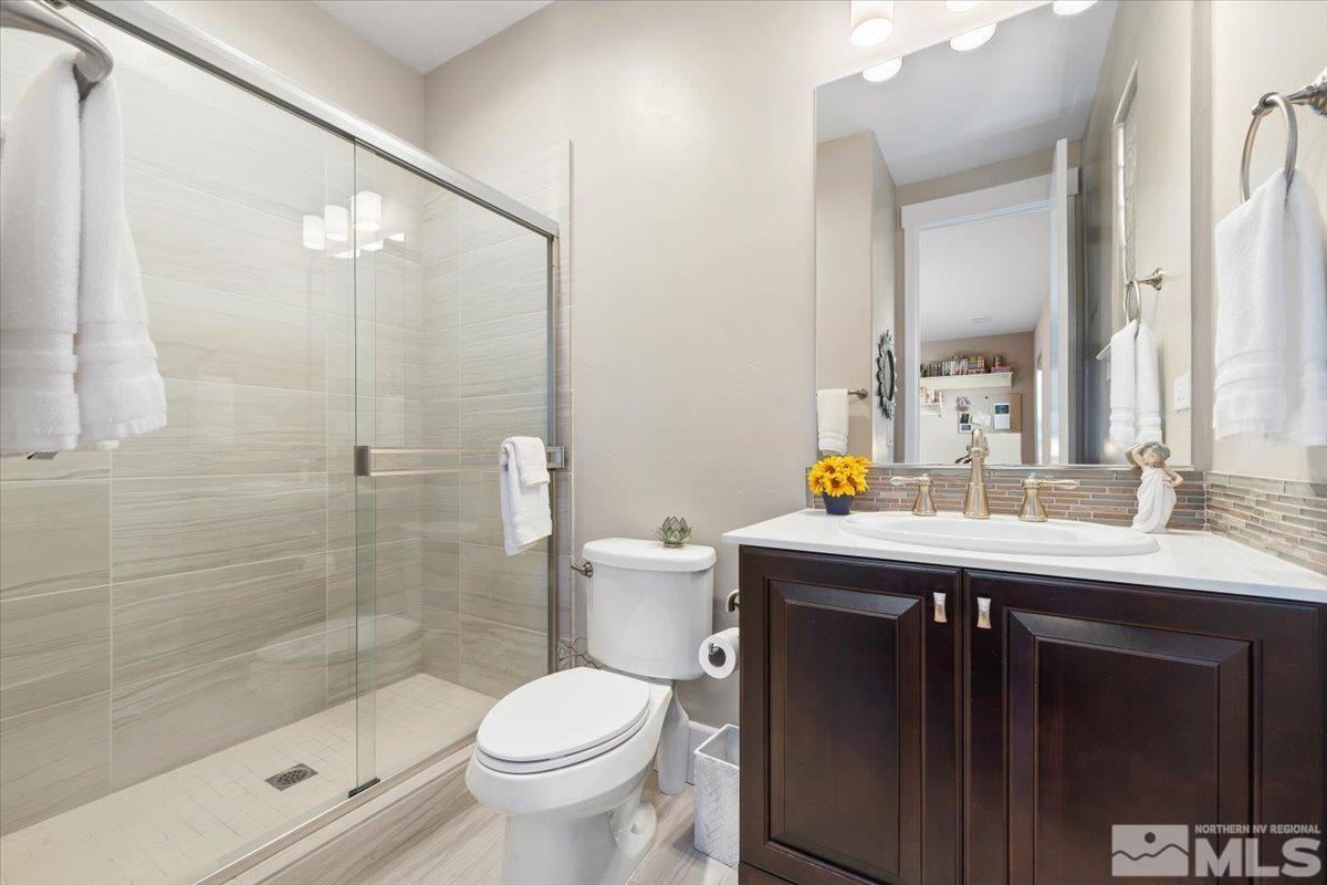 bathroom with toilet, an enclosed shower, backsplash, and vanity