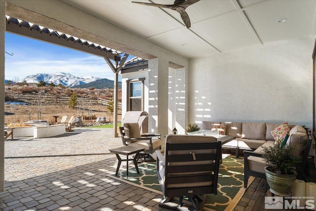 view of patio featuring ceiling fan, an outdoor living space with a fire pit, and a mountain view