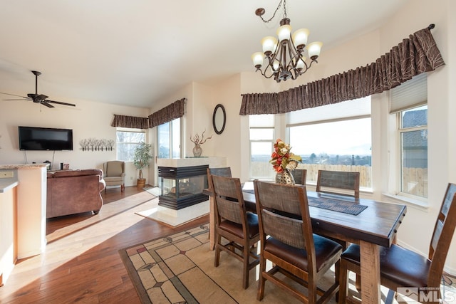 dining area with ceiling fan with notable chandelier, a tile fireplace, and light wood-type flooring