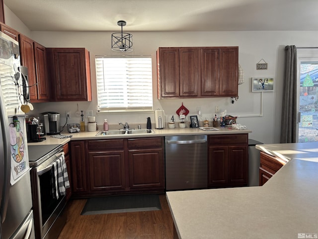 kitchen featuring appliances with stainless steel finishes, a healthy amount of sunlight, dark wood-type flooring, sink, and decorative light fixtures