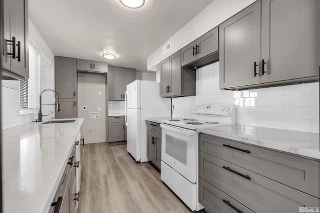 kitchen featuring light stone counters, sink, white appliances, and gray cabinets