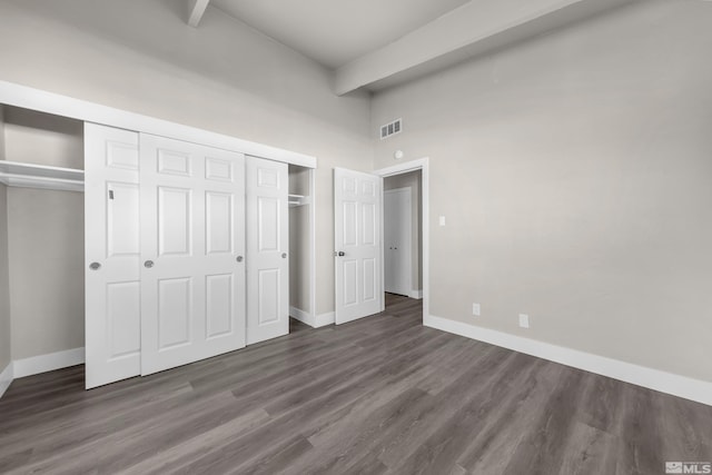 unfurnished bedroom featuring dark hardwood / wood-style flooring, beamed ceiling, and a towering ceiling