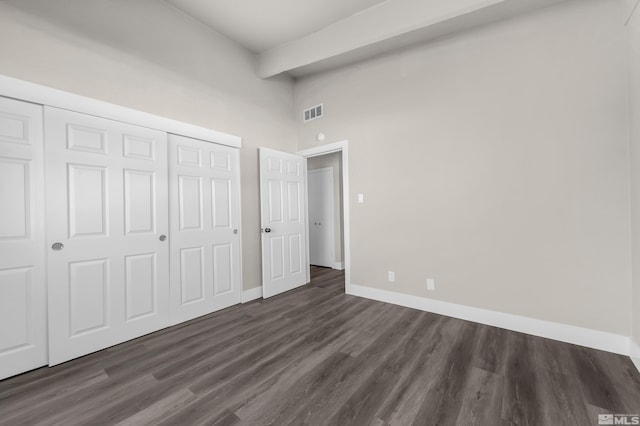 unfurnished bedroom with a closet, a towering ceiling, and dark hardwood / wood-style floors