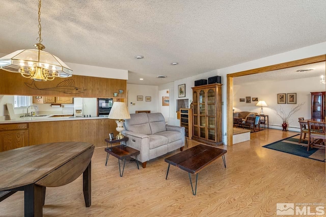 living room featuring a textured ceiling, light hardwood / wood-style flooring, sink, and a chandelier