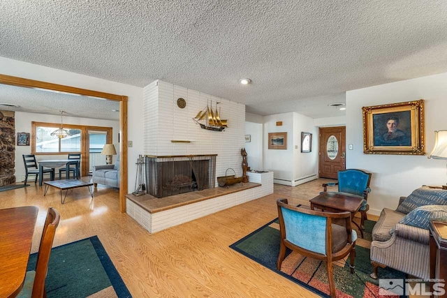 living room with a brick fireplace, a textured ceiling, and wood-type flooring