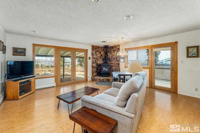 living room with a baseboard radiator, a textured ceiling, a healthy amount of sunlight, and a wood stove