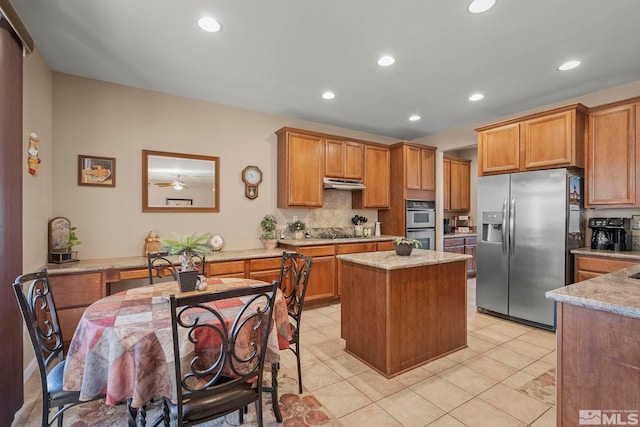 kitchen featuring stainless steel appliances, a center island, light stone countertops, decorative backsplash, and light tile patterned flooring