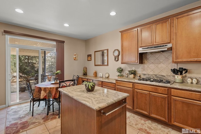 kitchen featuring light tile patterned floors, stainless steel gas stovetop, backsplash, light stone countertops, and a kitchen island