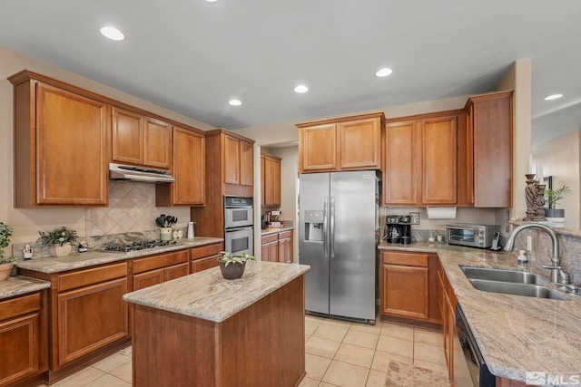 kitchen with sink, stainless steel appliances, a center island, and light stone counters