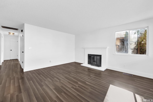 unfurnished living room featuring dark hardwood / wood-style flooring, a brick fireplace, and a textured ceiling