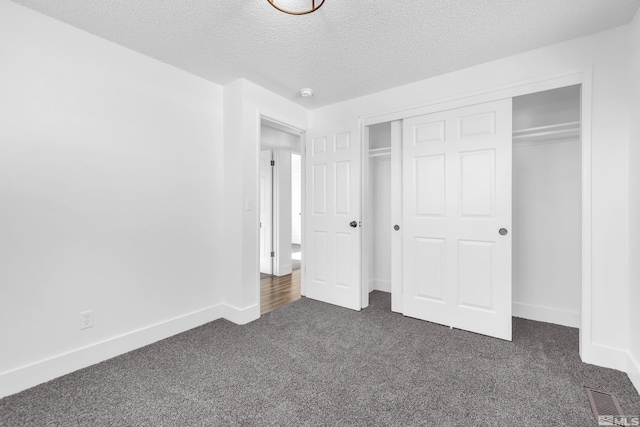 unfurnished bedroom featuring a textured ceiling, a closet, and dark colored carpet