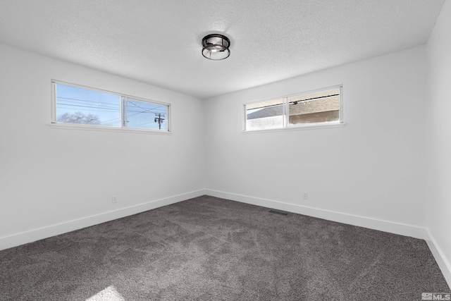 spare room with a textured ceiling, a wealth of natural light, and dark colored carpet