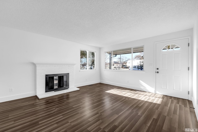 unfurnished living room with a brick fireplace, a textured ceiling, and dark hardwood / wood-style floors